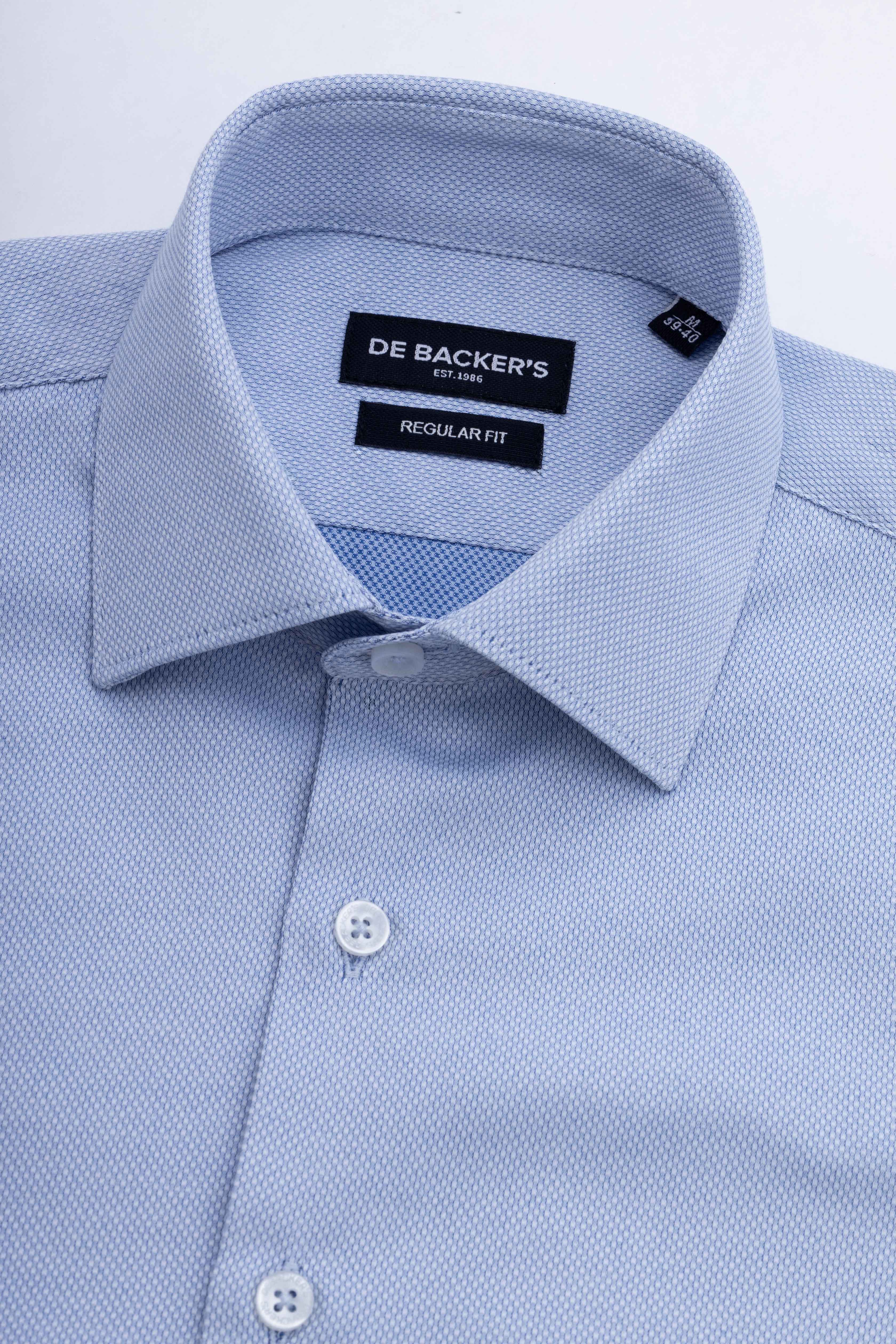 Close-up of a light blue piqué dress shirt by De Backer's, showing the collar, inner neck label, and front buttons on a white background.