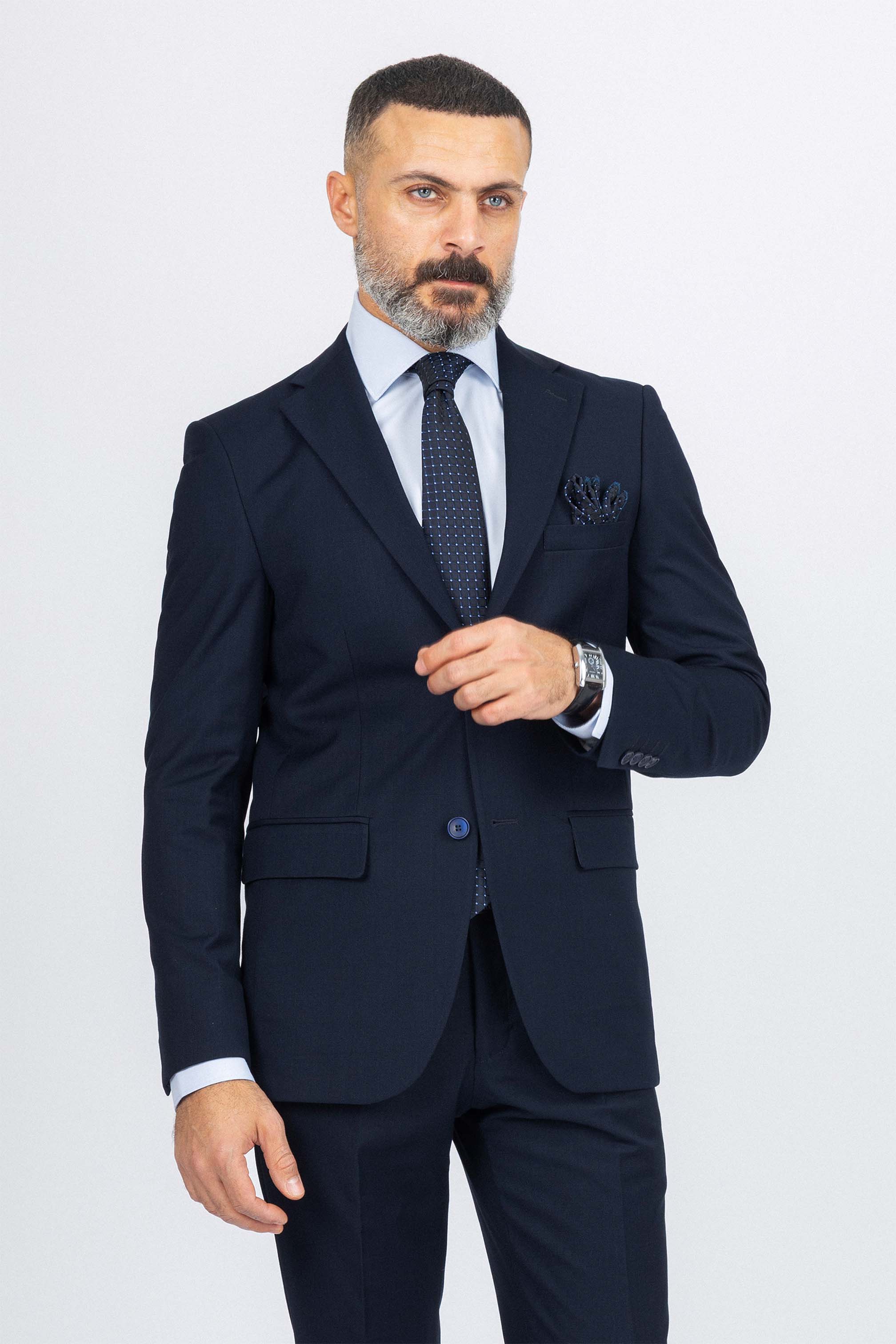 Man wearing a navy suit with a white shirt and patterned tie on a light gray background