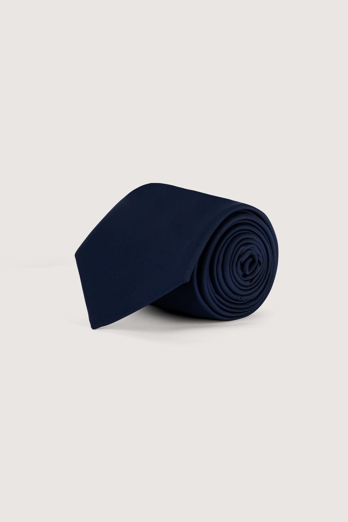 A rolled navy blue necktie displayed on a clean, light beige background.