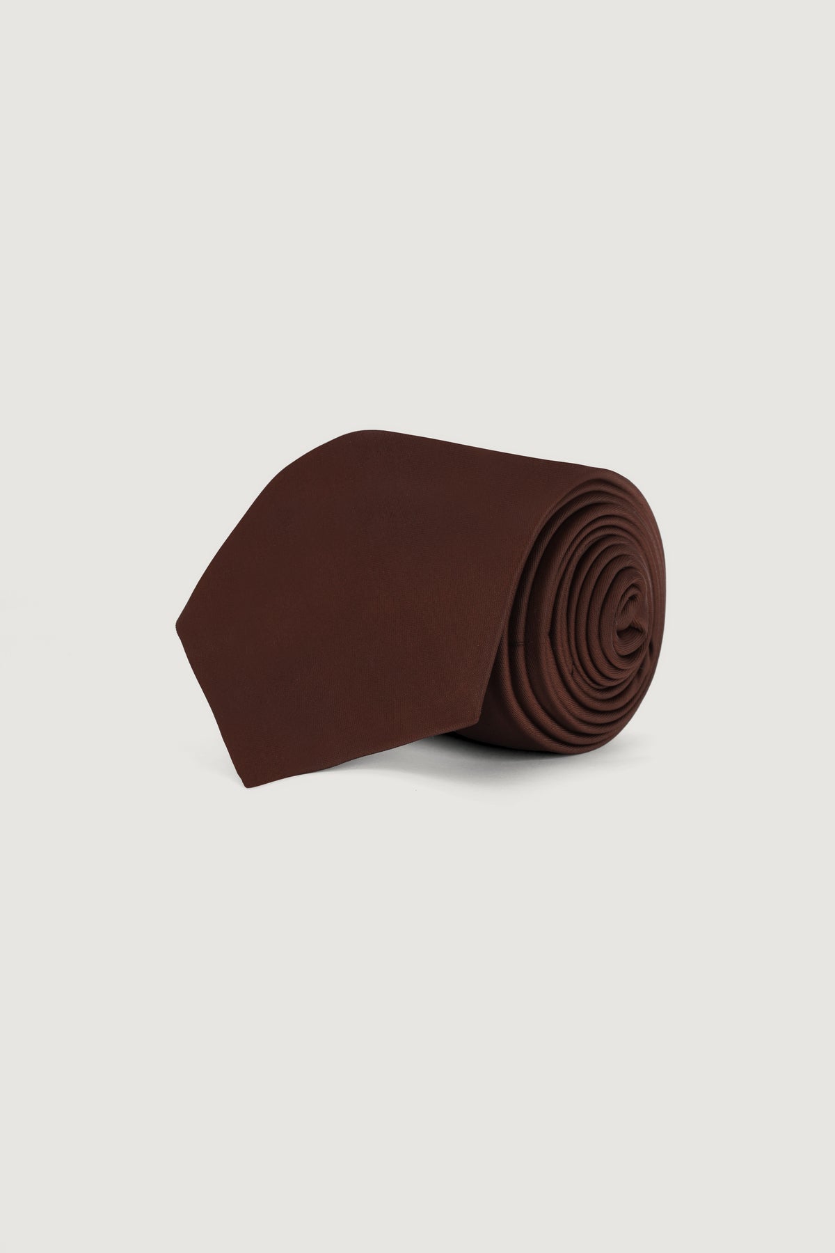 A rolled-up dark brown silk necktie on a light gray background.