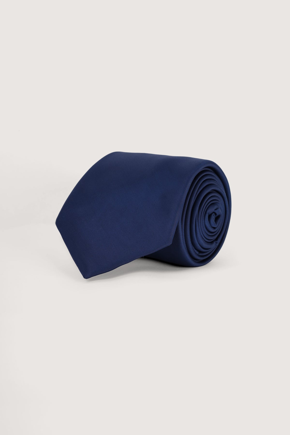 A rolled navy blue necktie displayed on a clean, light gray studio background.