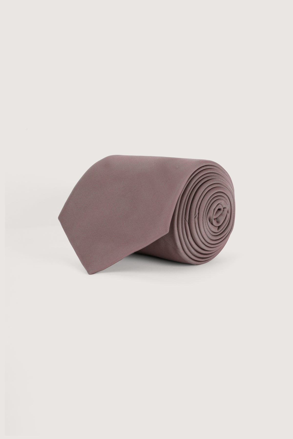 A rolled-up dusty mauve-purple necktie on a clean, light off-white background.